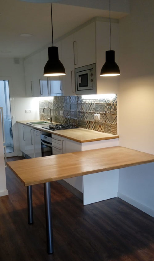 Cocina abierta con barra de madera, muebles blancos y lámparas colgantes