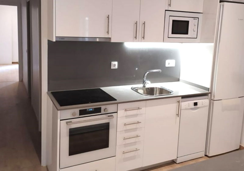 Cocina con muebles blancos, horno, placa de cocción y fregadero